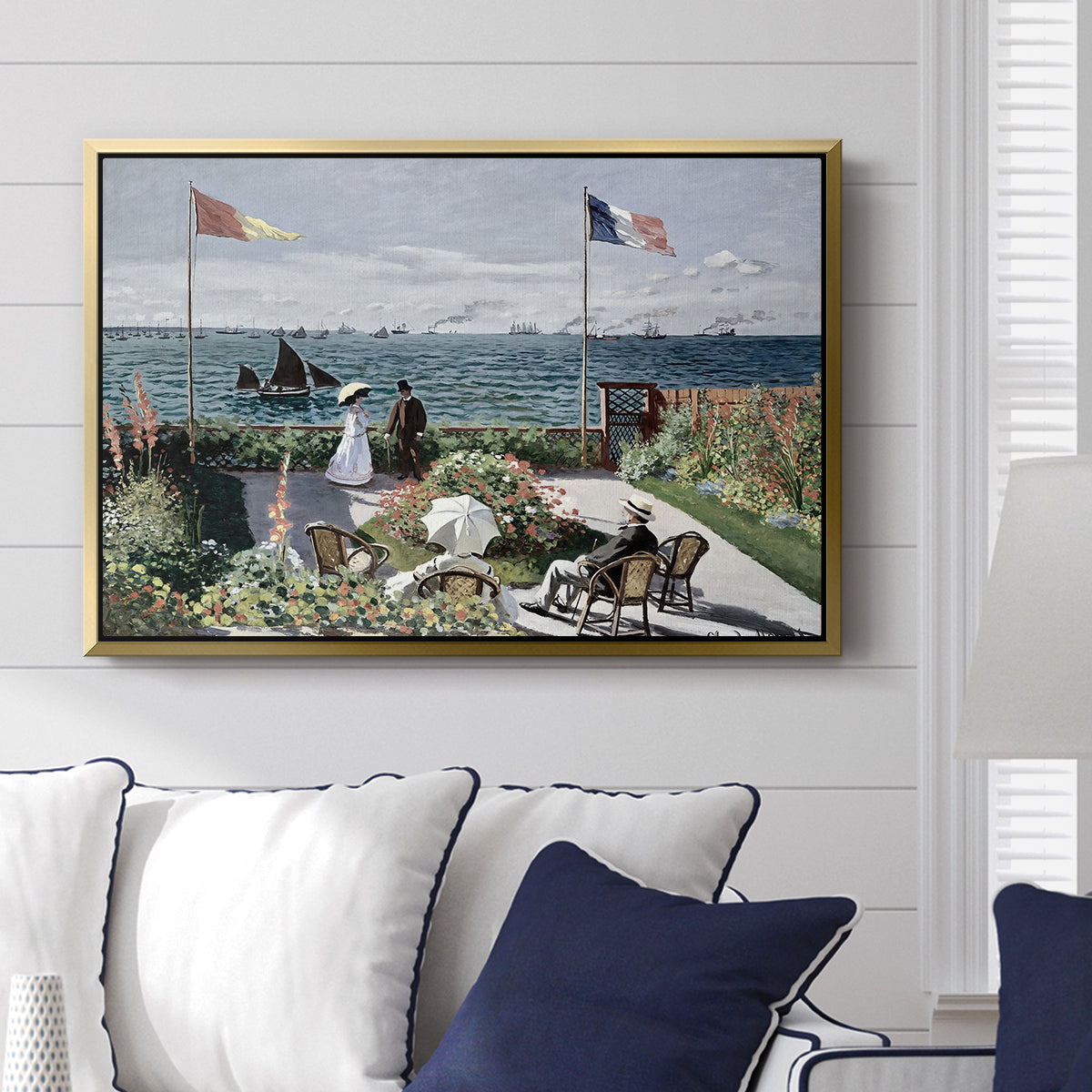 Garden at Sainte-Adresse, 1867 by Claude Monet displayed above a sofa in a living room in a gold floater frame, featuring an impressionist coastal garden with people and ocean view.