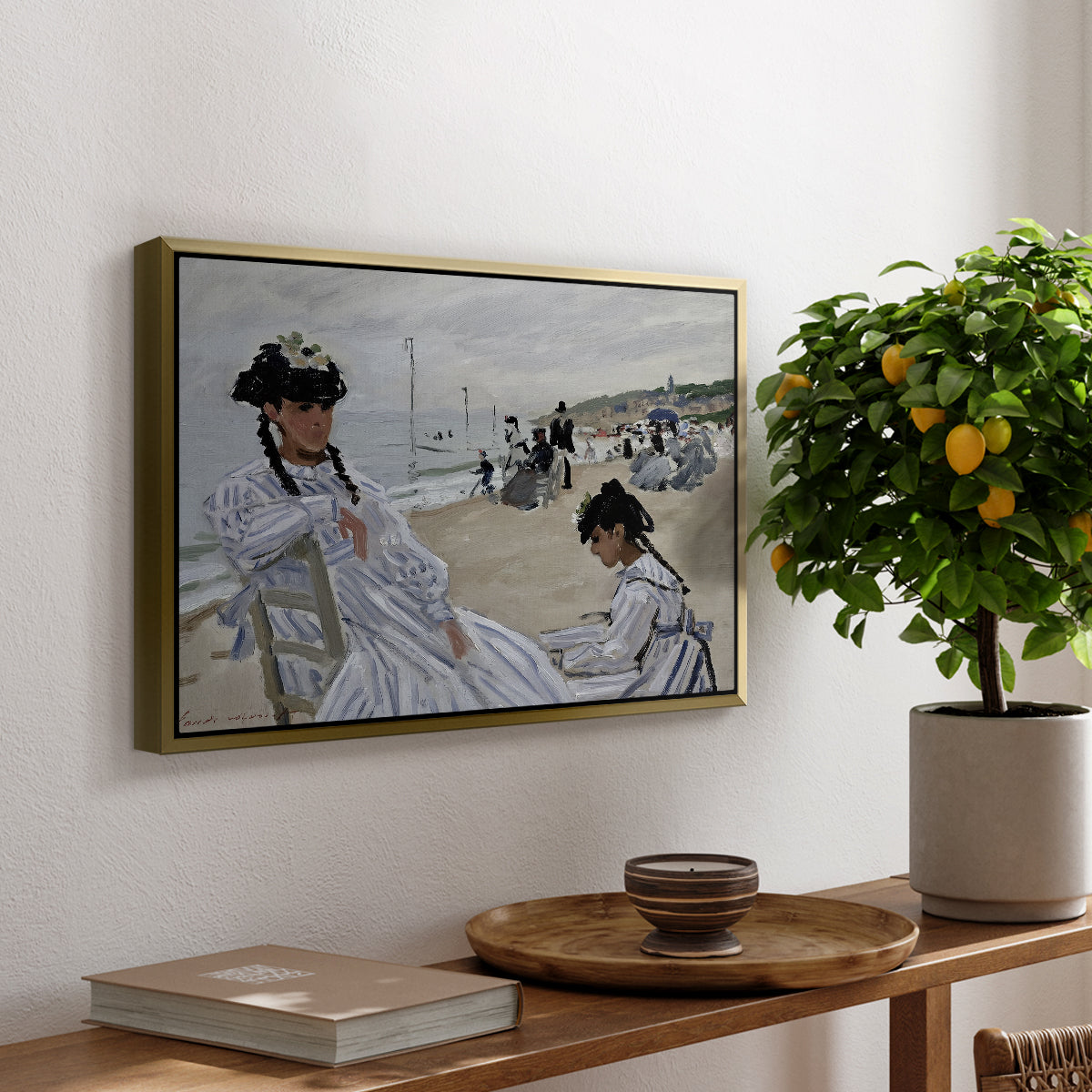 On the Beach at Trouville, 1870 by Claude Monet, presented in a gold floater framed canvas featuring figures seated on beach with parasols facing the ocean, displayed above a hallway console table.