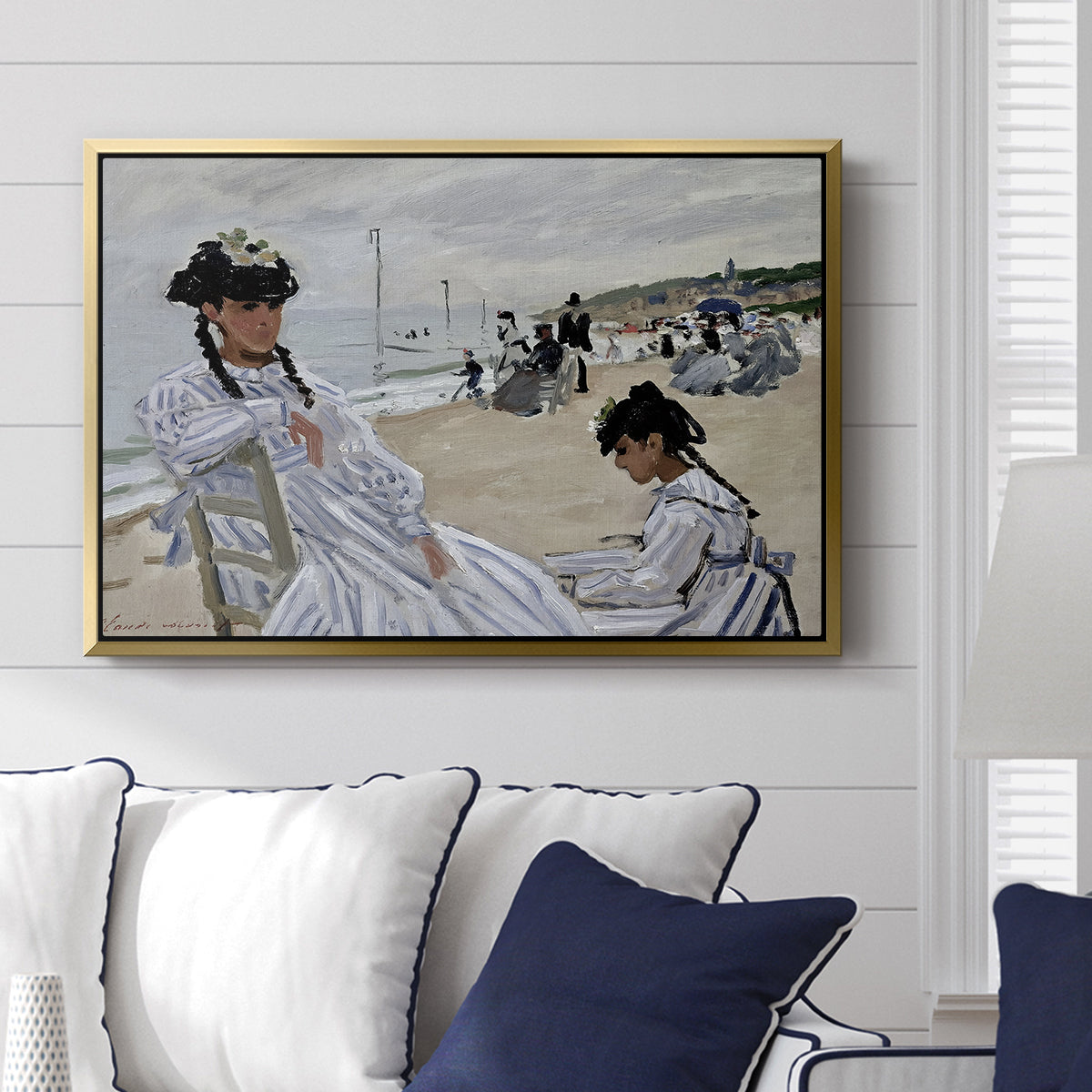 On the Beach at Trouville, 1870 by Claude Monet displayed above a sofa in a living room in a gold floater frame, featuring an impressionist seaside scene with women in dresses and hats.