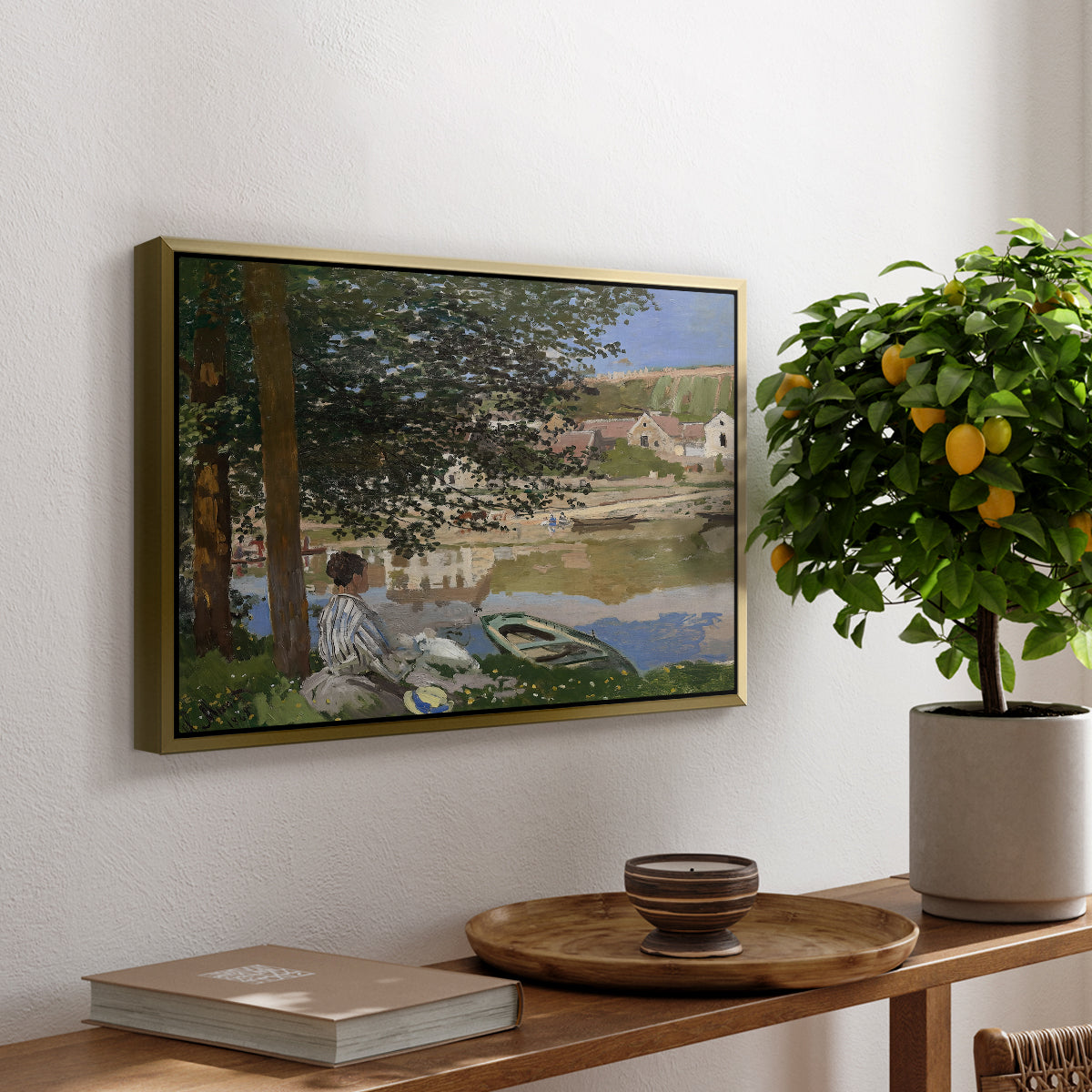 On the Bank of the Seine, Bennecourt, 1868 by Claude Monet, presented in a gold floater framed canvas featuring a woman and child seated along riverbank beneath trees in soft daylight, displayed above a hallway console table.