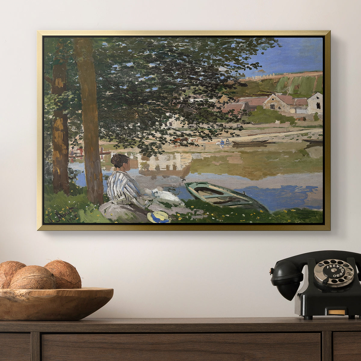 On the Bank of the Seine, Bennecourt, 1868 by Claude Monet in a gold floater framed canvas displayed above a console table in a hallway, featuring a quiet outdoor setting with figures near river under foliage.