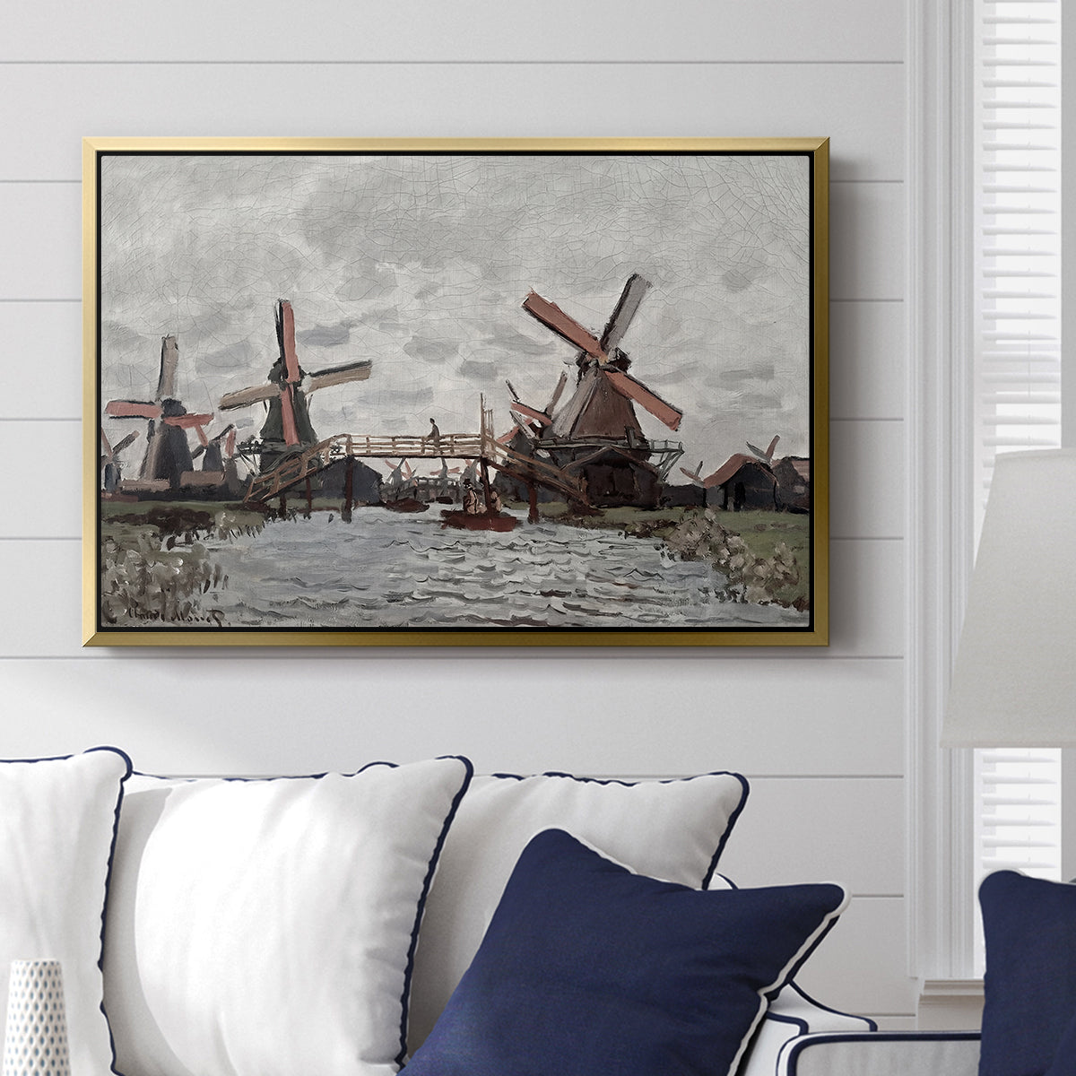 Windmills near Zaandam, 1871 by Claude Monet displayed above a sofa in a living room in a gold floater frame, featuring an impressionist view of Dutch windmills along riverbank.
