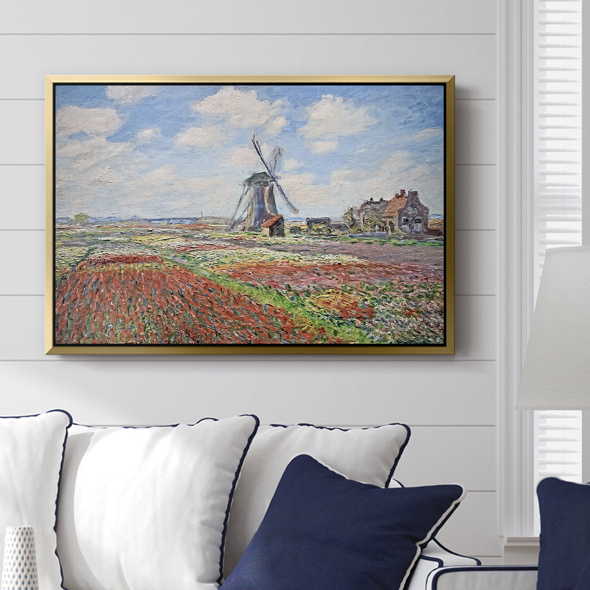 Tulip Fields with the Rijnsburg Windmill, 1886 by Claude Monet displayed above a sofa in a living room in a gold floater frame, featuring a vibrant agricultural landscape with flowers and windmill.