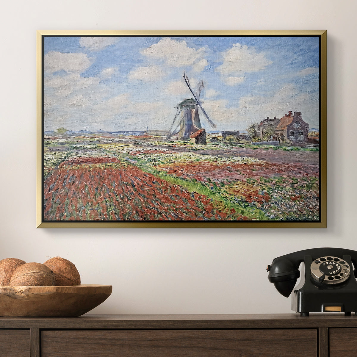 Tulip Fields with the Rijnsburg Windmill, 1886 by Claude Monet in a gold floater framed canvas displayed above a console table in a hallway, featuring a rural scene with patterned rows of flowers and windmill.