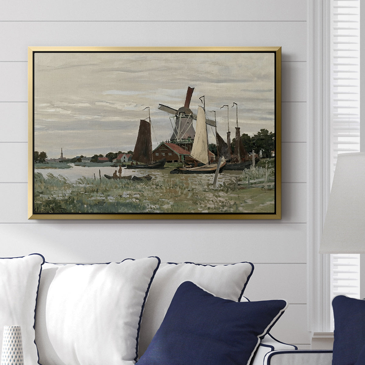 Windmill at Zaandam, 1871 by Claude Monet displayed above a sofa in a living room in a gold floater frame, featuring an impressionist depiction of windmill near riverbank.