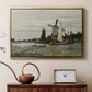 Gold floater framed canvas featuring a rustic scene with windmill and reflections in water, displayed above a cabinet in a soft-toned living room.