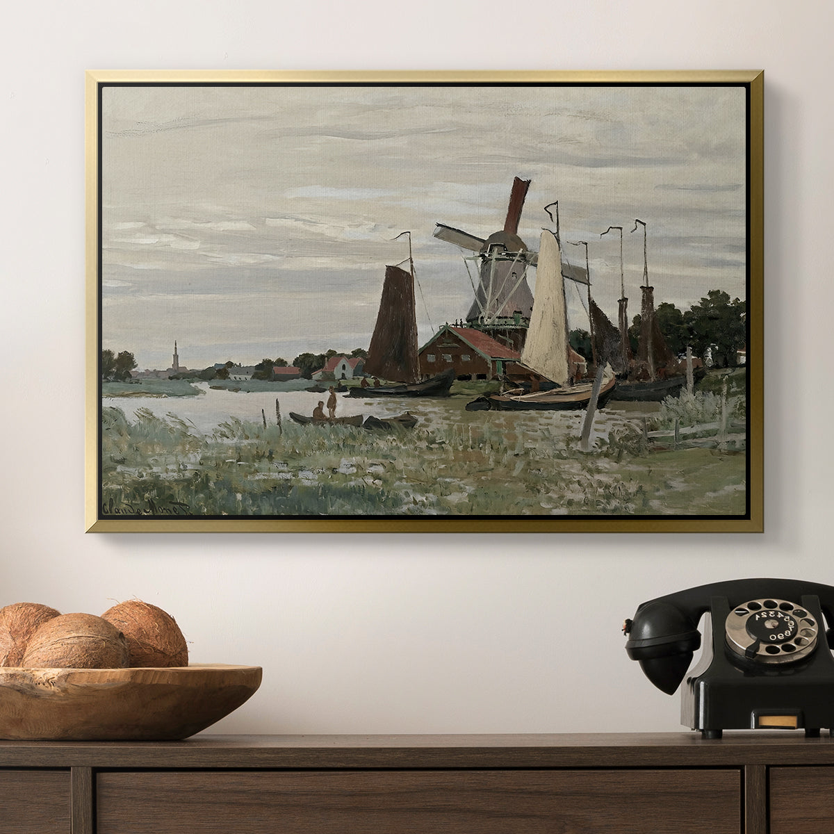 Windmill at Zaandam, 1871 by Claude Monet in a gold floater framed canvas displayed above a console table in a hallway, featuring a countryside structure standing against open sky.