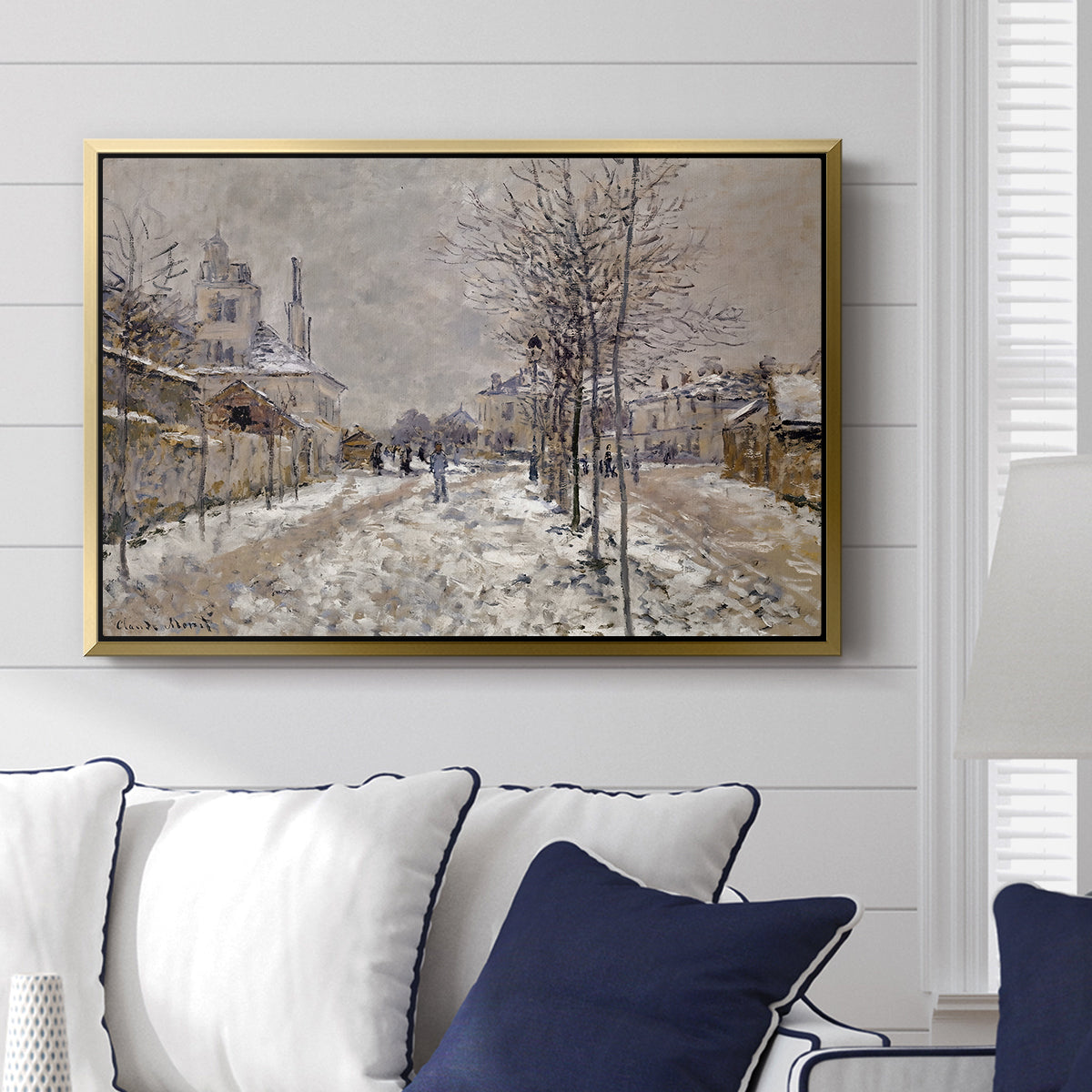 The Boulevard de Pontoise at Argenteuil, Snow Effect, 1875 by Claude Monet displayed above a sofa in a living room in a gold floater frame, featuring an impressionist winter scene with road and bare trees.
