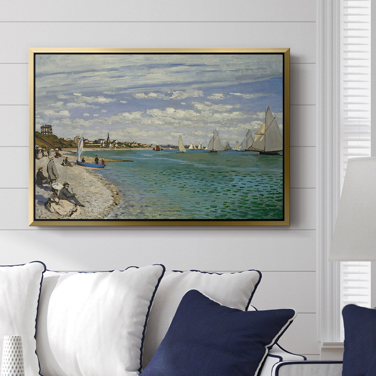 Regatta at Sainte-Adresse, 1867 by Claude Monet displayed above a sofa in a living room in a gold floater frame, featuring a lively regatta scene with boats and people on beach.