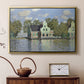 Gold floater framed canvas featuring a peaceful canal scene with houses mirrored in water, displayed above a cabinet in a soft-toned living room.