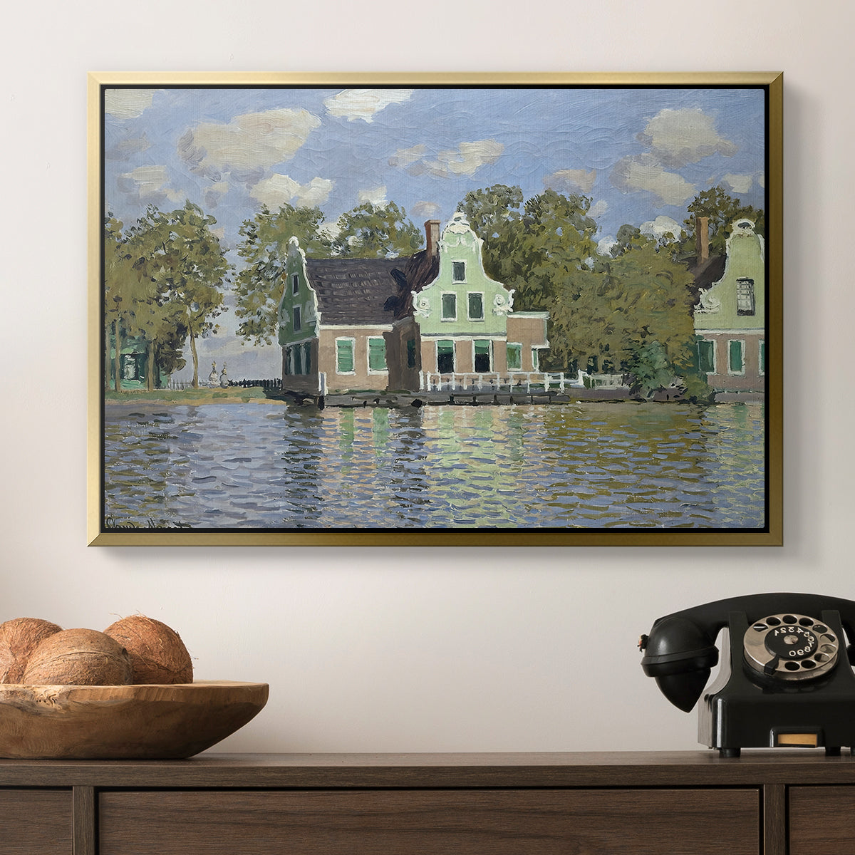 Houses on the Zaan River at Zaandam, 1871 by Claude Monet in a gold floater framed canvas displayed above a console table in a hallway, featuring a waterfront architecture with still reflections.