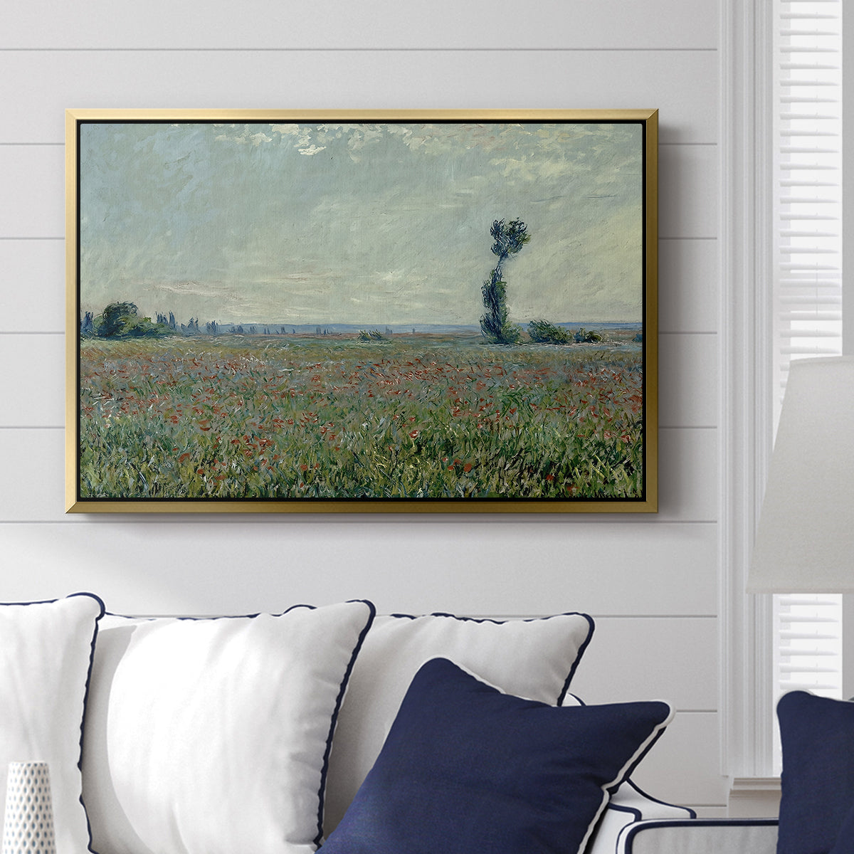 Poppy Field, 1881 by Claude Monet displayed above a sofa in a living room in a gold floater frame, featuring an impressionist landscape filled with blooming flowers and greenery.