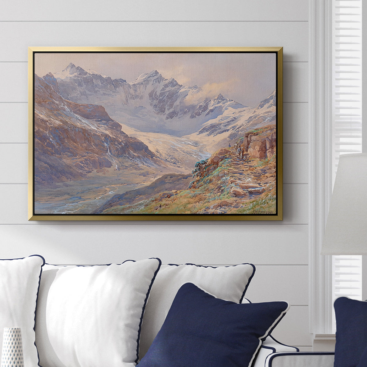 Odenwinklkees with the Johannisberg, 1902 by Edward Theodore Compton displayed above a sofa in a living room in a gold floater frame, featuring a mountain scene with glacier stretching through rocky valley.