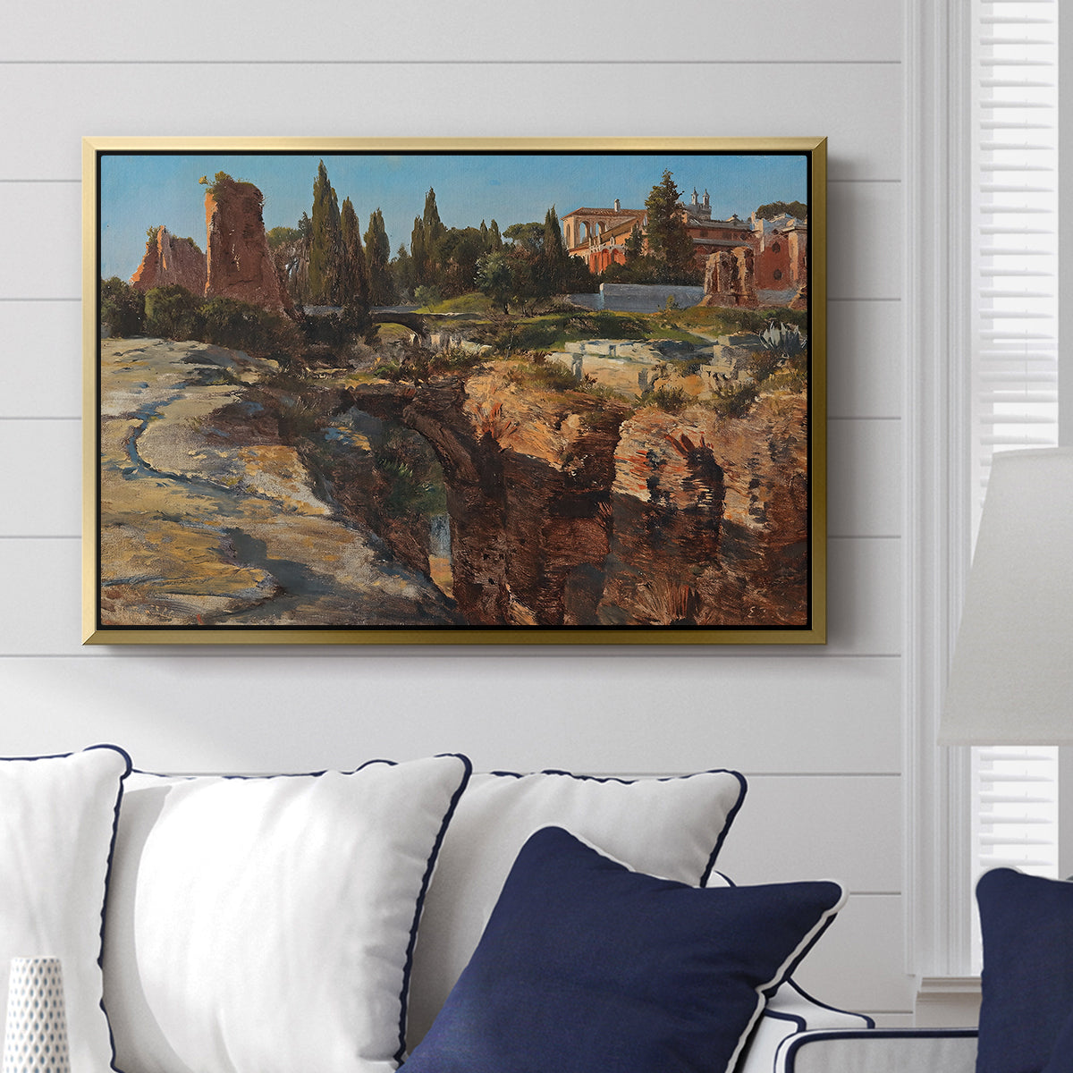 Palatine in Rome, c. 1921 by Edward Theodore Compton displayed above a sofa in a living room in a gold floater frame, featuring an architectural scene of ancient structures in sunlit environment.