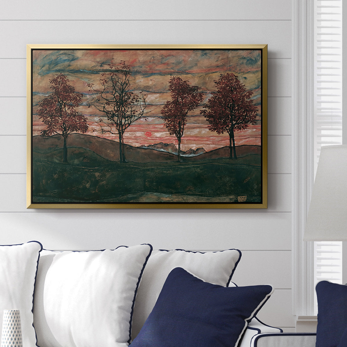 Four Trees, 1917 by Egon Schiele displayed above a sofa in a living room in a gold floater frame, featuring a minimal landscape with grouped trees and expressive color.