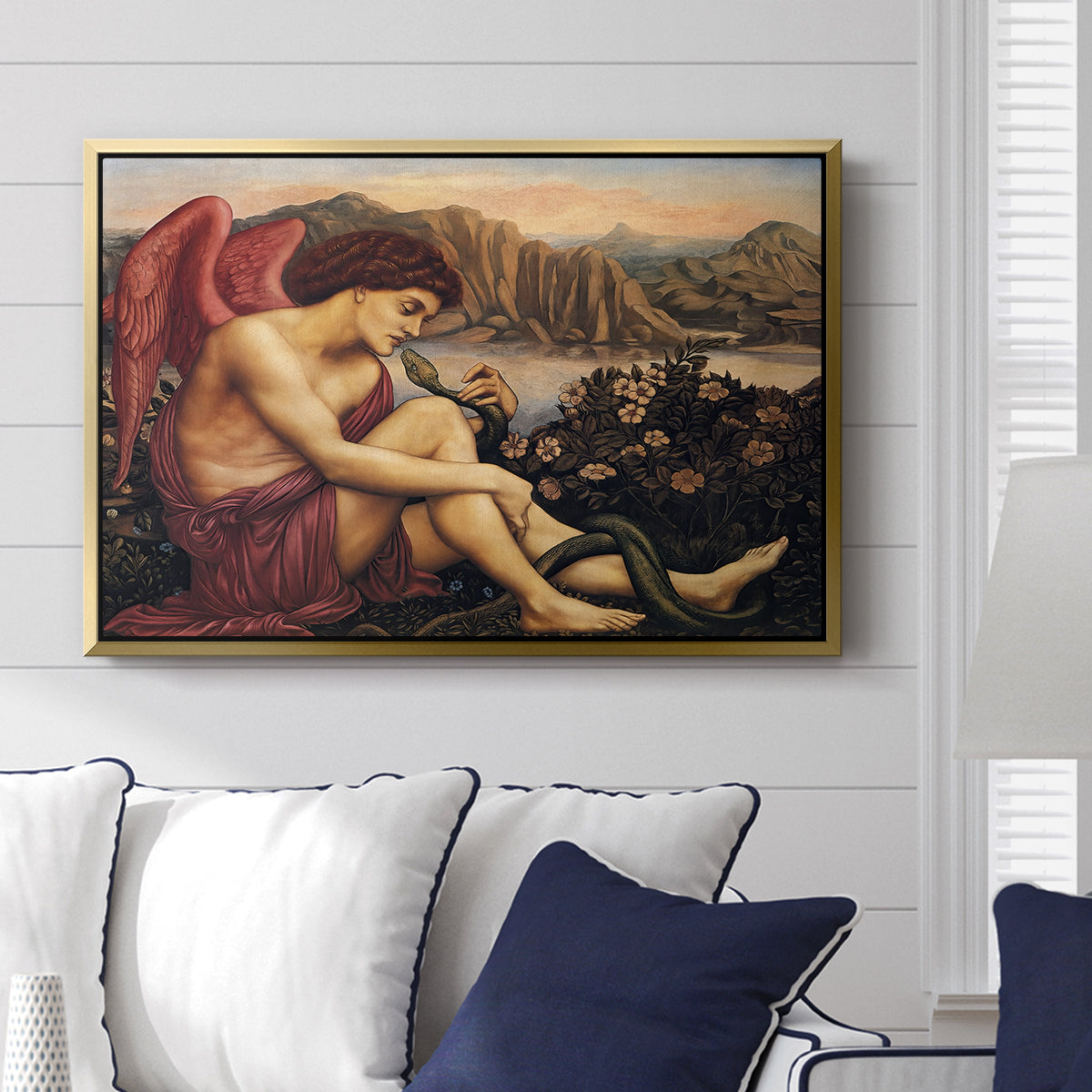 The Angel with the Serpent, c. 1870-1875 by Evelyn De Morgan displayed above a sofa in a living room in a gold floater frame, featuring a winged figure standing over serpent in allegorical composition.