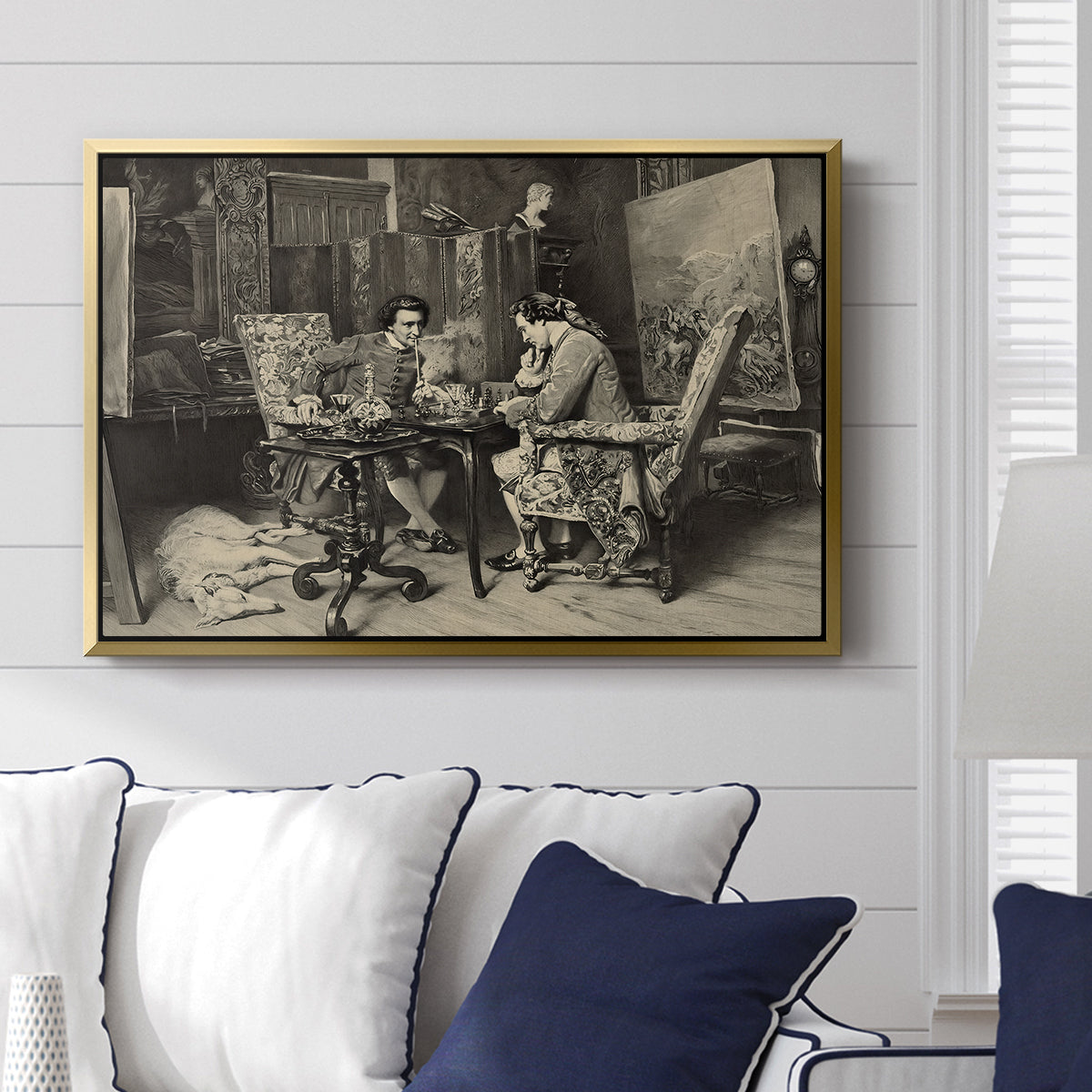 The Chess Players, 1858 by Ernest Meissonier displayed above a sofa in a living room in a gold floater frame, featuring a realistic scene of figures concentrating on chess game indoors.