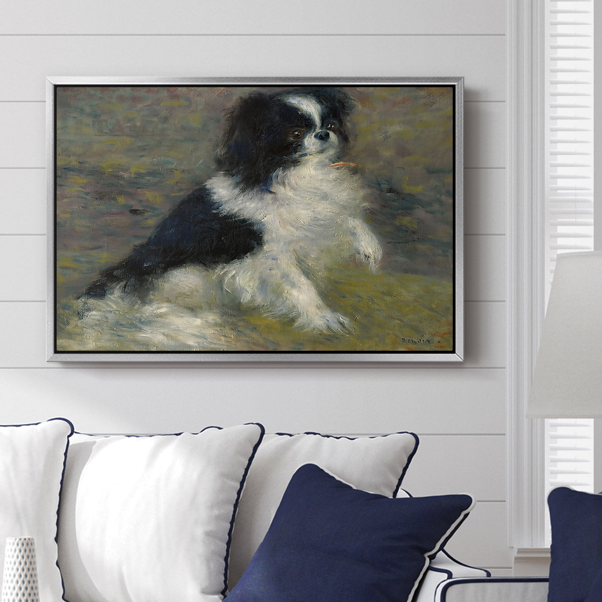 Tama, the Japanese Dog, c. 1876 by Pierre-Auguste Renoir displayed above a sofa in a living room in a silver floater frame, featuring an impressionist painting of a dog wading through water with blurred background.