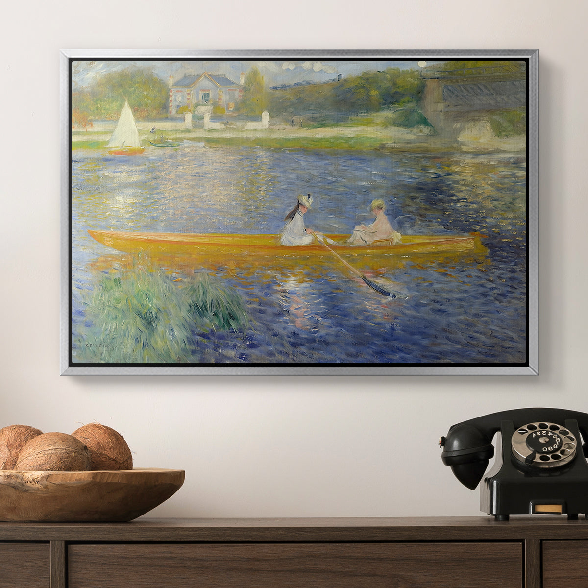 The Skiff (La Yole), 1875 by Pierre-Auguste Renoir in a silver floater framed canvas displayed above a console table in a hallway, featuring a leisure scene of figures in a small rowboat on tranquil water.