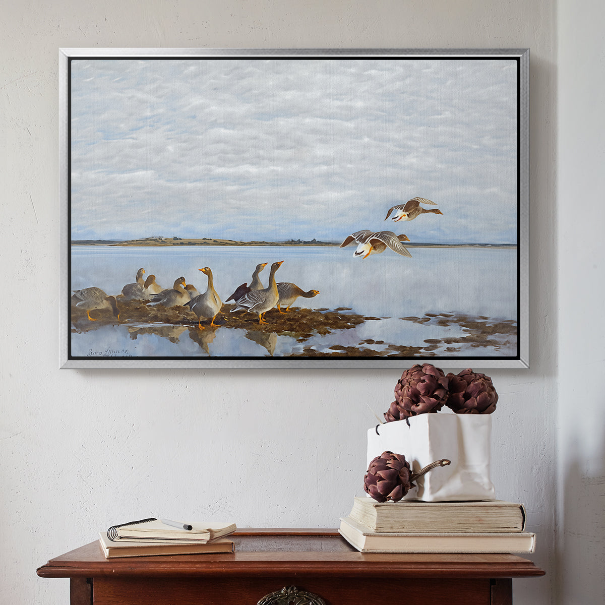 Silver floater framed canvas featuring Greylag Geese (Grågäss), 1922 by Bruno Liljefors above an entryway table in a minimalist foyer.