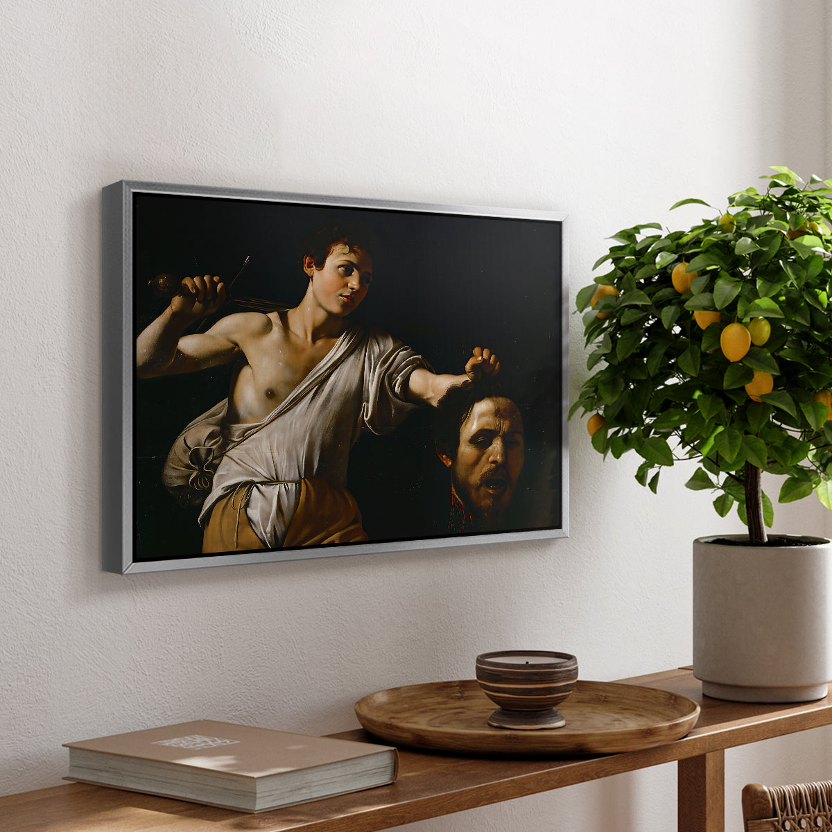 David with the Head of Goliath (Vienna Version), c. 1607 by Caravaggio, presented in a silver floater framed canvas featuring a young David holding the severed head of Goliath against a dark background, displayed above a hallway console table.