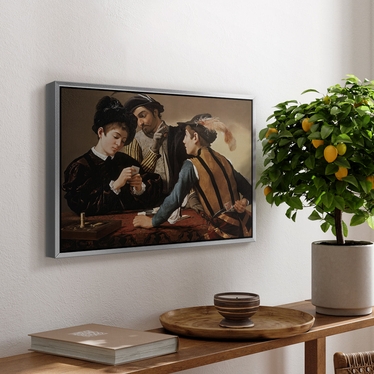 The Cardsharps, c. 1594 by Caravaggio, presented in a silver floater framed canvas featuring two men cheating at cards while a third figure secretly observes behind them, displayed above a hallway console table.