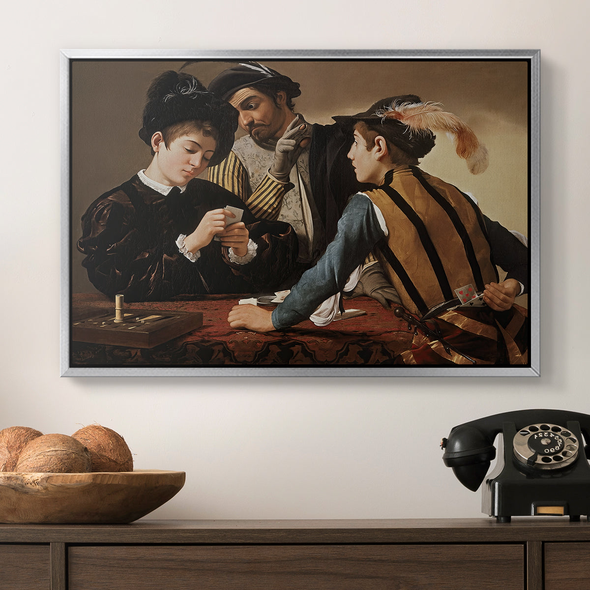 The Cardsharps, c. 1594 by Caravaggio in a silver floater framed canvas displayed above a console table in a hallway, featuring a dramatic interior scene of gambling and trickery among figures.