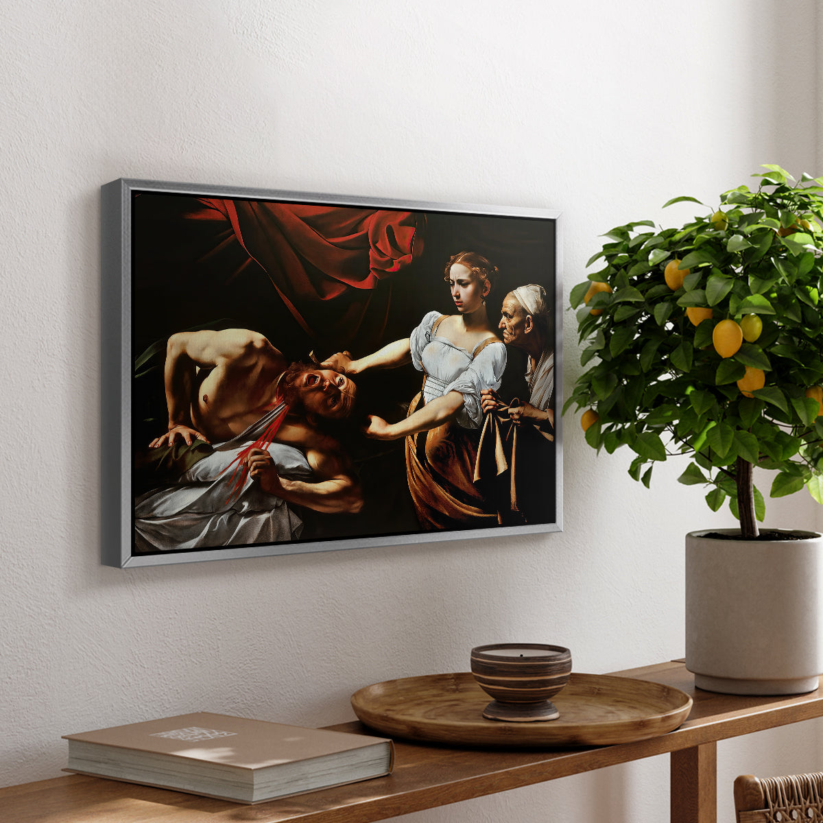 Judith Beheading Holofernes, c. 1599 by Caravaggio, presented in a silver floater framed canvas featuring Judith cutting off Holofernes' head as maidservant assists beside her, displayed above a hallway console table.
