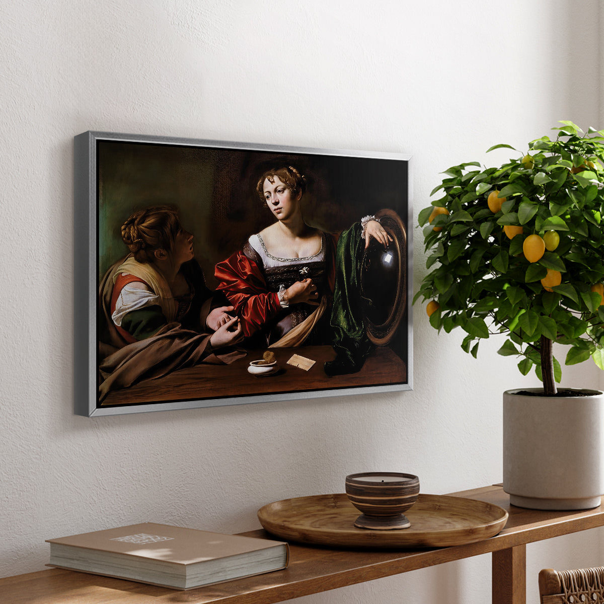 Martha and Mary Magdalene, c. 1598 by Caravaggio, presented in a silver floater framed canvas featuring a two women seated together in conversation with symbolic objects on table, displayed above a hallway console table.