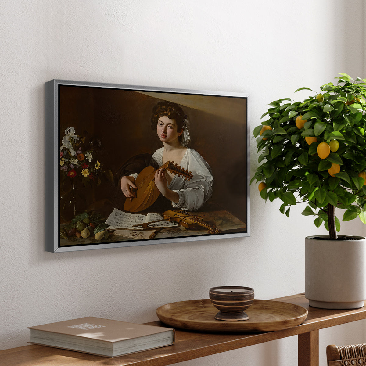 The Lute Player (Hermitage Version), c. 1596 by Caravaggio, presented in a silver floater framed canvas featuring a young musician playing lute beside table with fruit and sheet music, displayed above a hallway console table.