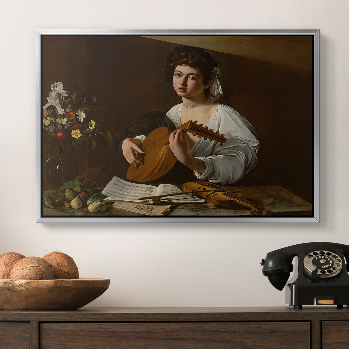 The Lute Player (Hermitage Version), c. 1596 by Caravaggio in a silver floater framed canvas displayed above a console table in a hallway, featuring a Baroque depiction of musician with detailed textures and lighting.