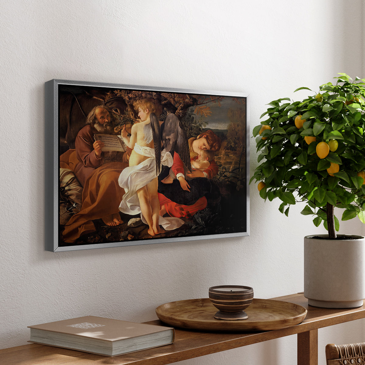 Rest on the Flight into Egypt, c. 1597 by Caravaggio, presented in a silver floater framed canvas featuring the Holy Family resting in landscape with angel playing violin, displayed above a hallway console table.