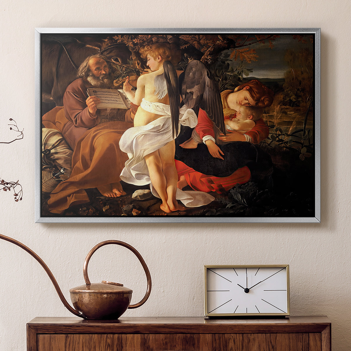 Silver floater framed canvas featuring a peaceful religious moment with figures reclining in natural setting, displayed above a cabinet in a soft-toned living room.