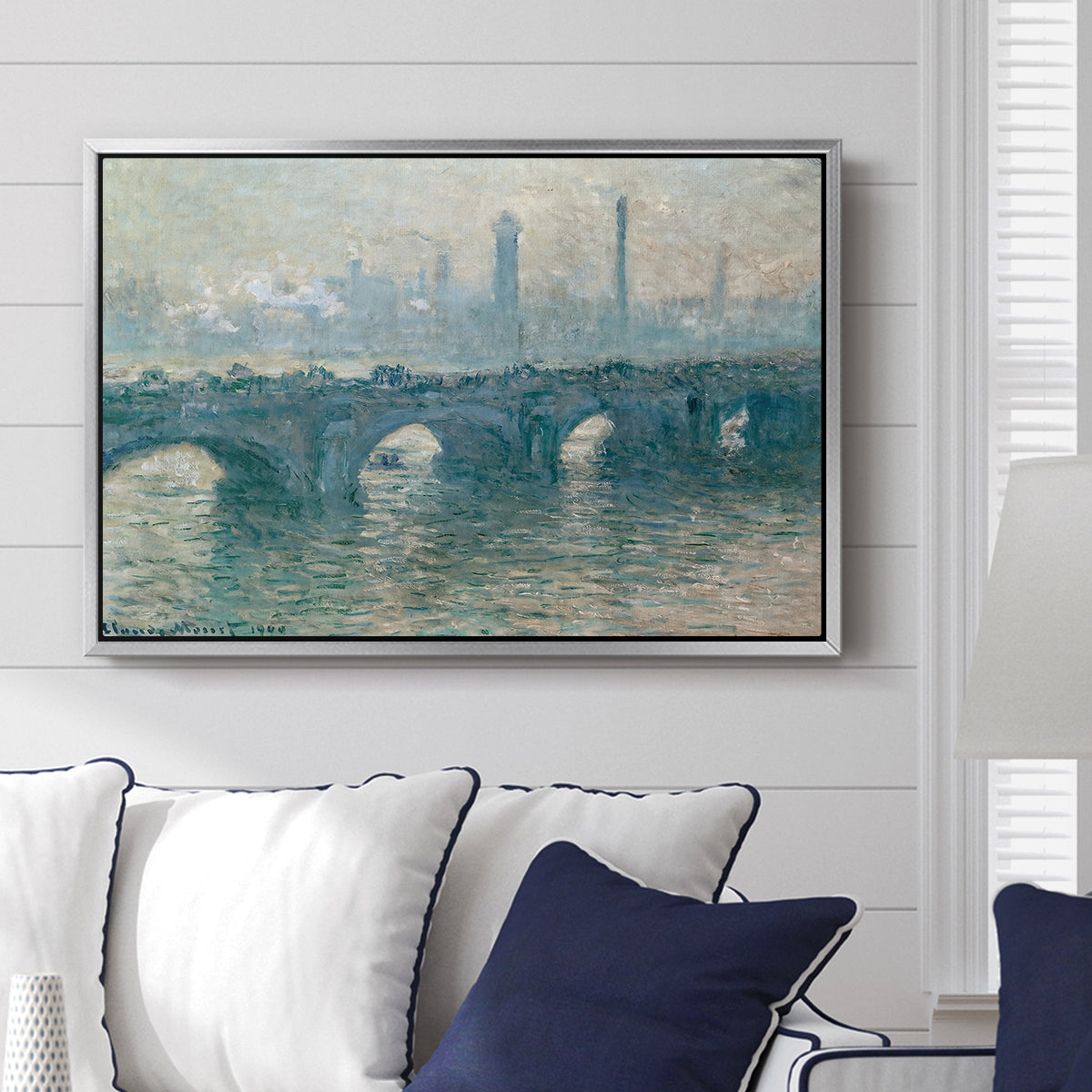 Waterloo Bridge, Gray Weather, 1900 by Claude Monet displayed above a sofa in a living room in a silver floater frame, featuring an impressionist cityscape with bridge fading into fog over water.
