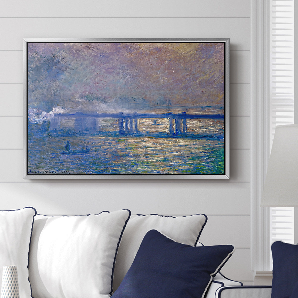 Charing Cross Bridge, 1903 by Claude Monet displayed above a sofa in a living room in a silver floater frame, featuring an urban landscape with bridge and water rendered in blurred tones.