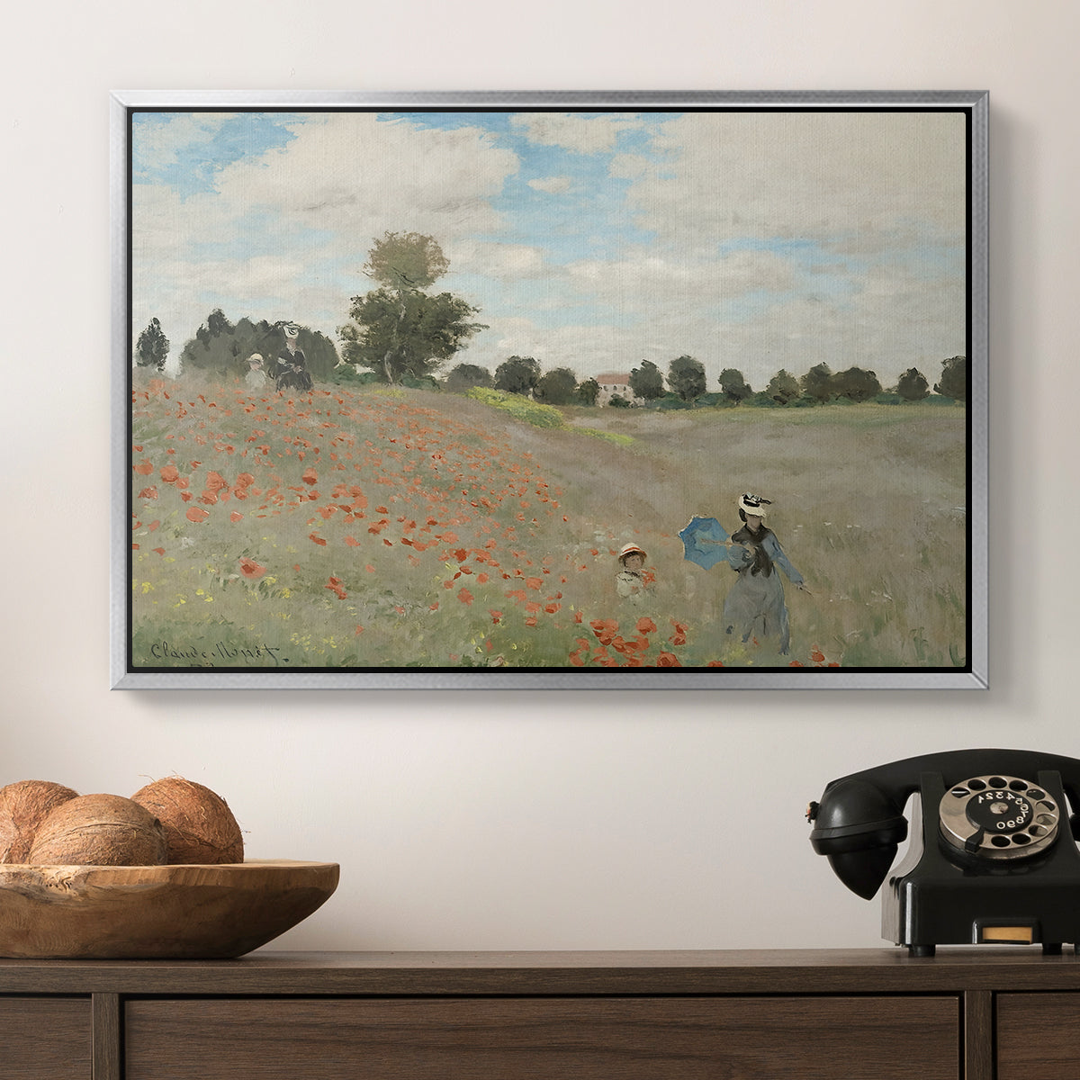 The Poppy Field near Argenteuil, 1873 by Claude Monet in a silver floater framed canvas displayed above a console table in a hallway, featuring a rural landscape with scattered figures among blooming flowers.