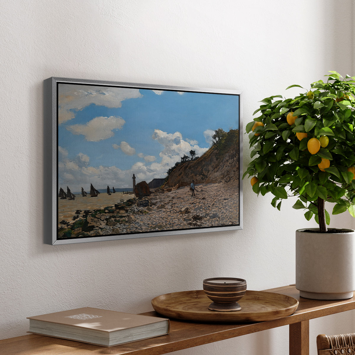 The Beach at Honfleur, 1864 by Claude Monet, presented in a silver floater framed canvas featuring a coastal beach scene with figures gathered along shoreline and boats nearby, displayed above a hallway console table.