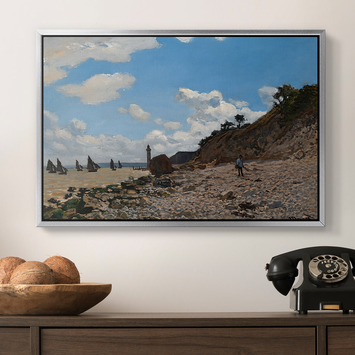 The Beach at Honfleur, 1864 by Claude Monet in a silver floater framed canvas displayed above a console table in a hallway, featuring a coastal landscape with boats and people along shore.