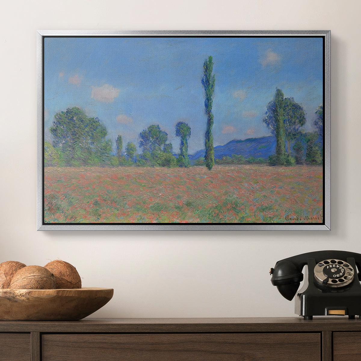 Poppy Field (Giverny), 1890-1891 by Claude Monet in a silver floater framed canvas displayed above a console table in a hallway, featuring a rural field filled with red blossoms beneath open sky.