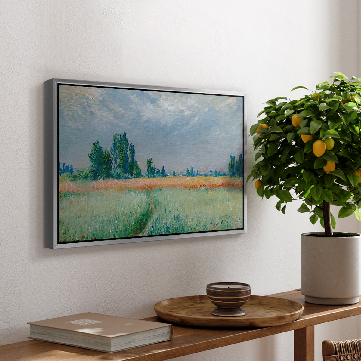 The Wheat Field (Champ de Blé), 1881 by Claude Monet, presented in a silver floater framed canvas featuring a golden wheat field stretching across landscape under soft sky, displayed above a hallway console table.