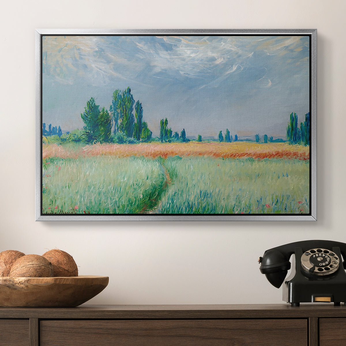 The Wheat Field (Champ de Blé), 1881 by Claude Monet in a silver floater framed canvas displayed above a console table in a hallway, featuring a serene rural scene with textured wheat under natural light.