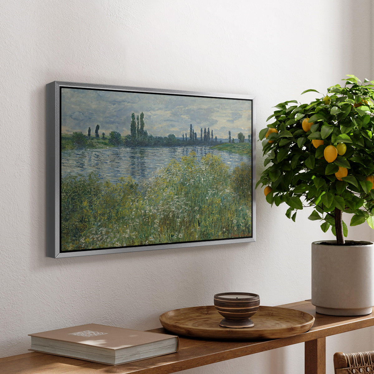 Banks of the Seine, Vétheuil, 1880 by Claude Monet, presented in a silver floater framed canvas featuring a riverbank landscape with water, trees, and distant village buildings, displayed above a hallway console table.