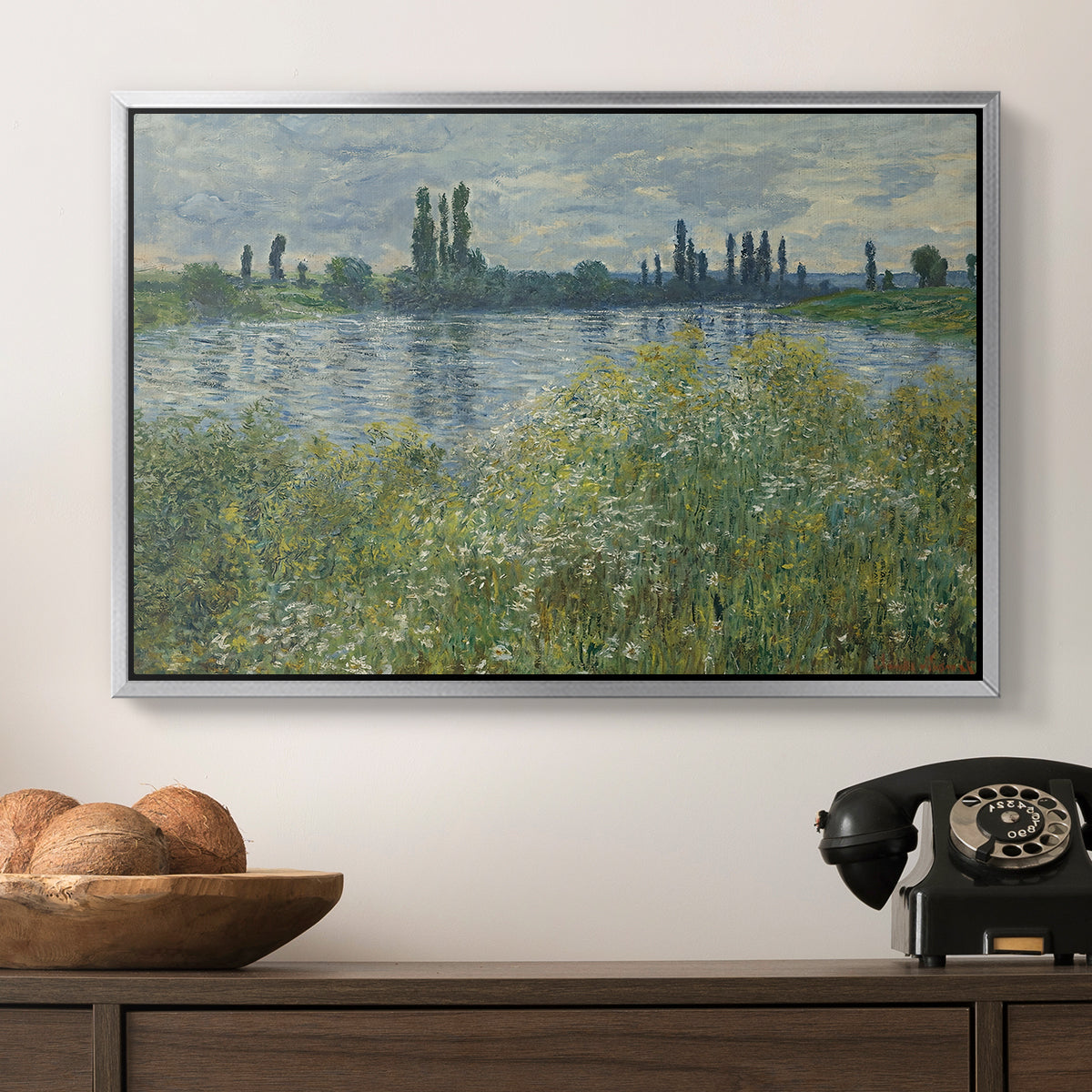 Banks of the Seine, Vétheuil, 1880 by Claude Monet in a silver floater framed canvas displayed above a console table in a hallway, featuring a natural landscape with calm water and soft foliage.