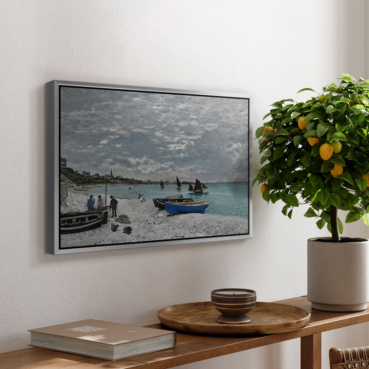 The Beach at Sainte-Adresse, 1867 by Claude Monet, presented in a silver floater framed canvas featuring a seaside promenade with figures, flags, and boats along the coast, displayed above a hallway console table.