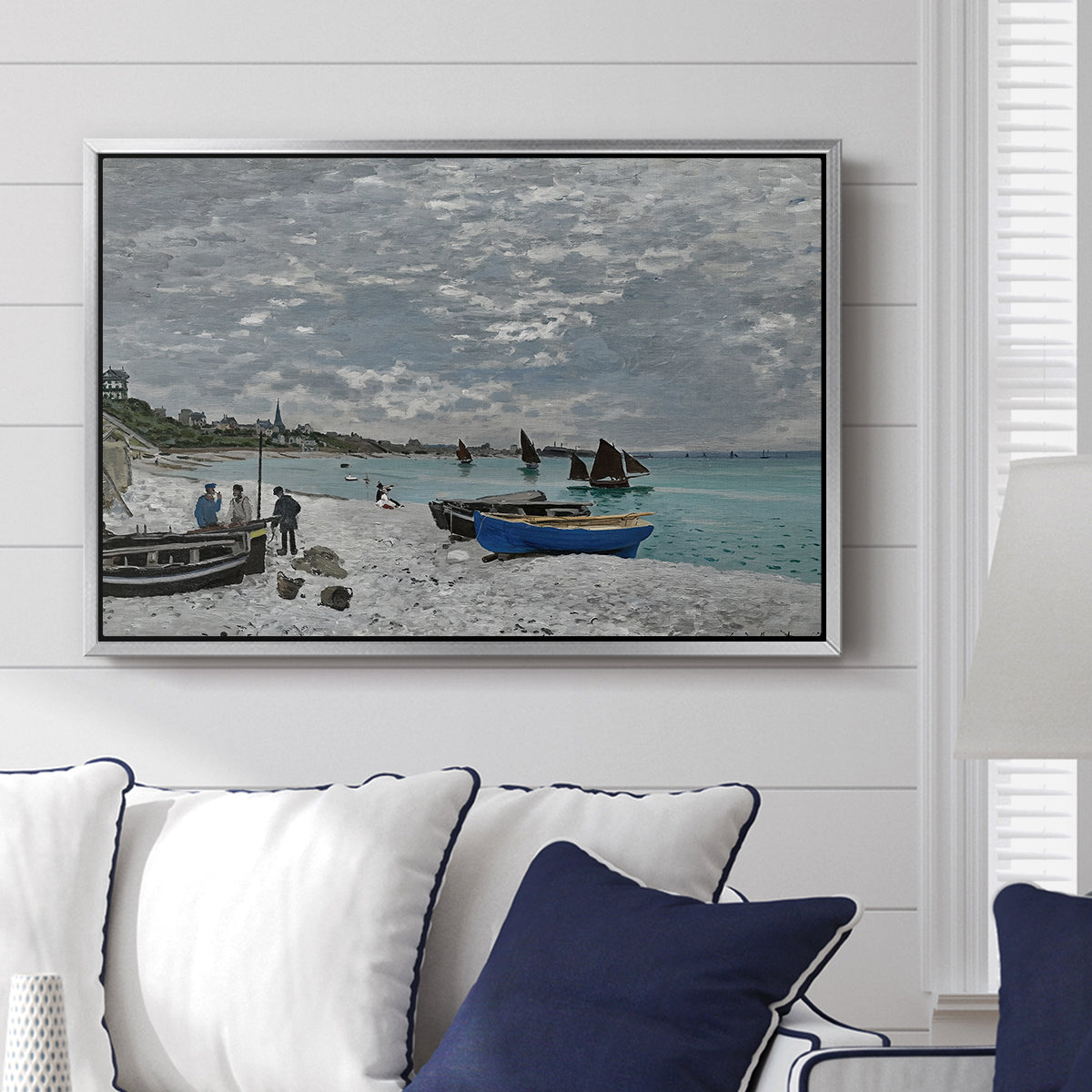 The Beach at Sainte-Adresse, 1867 by Claude Monet displayed above a sofa in a living room in a silver floater frame, featuring a lively beach scene with people overlooking water and ships.