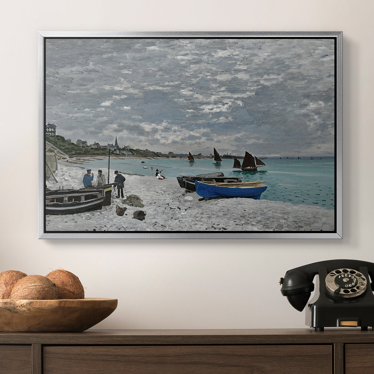 The Beach at Sainte-Adresse, 1867 by Claude Monet in a silver floater framed canvas displayed above a console table in a hallway, featuring an impressionist seaside gathering with flags and ocean view.