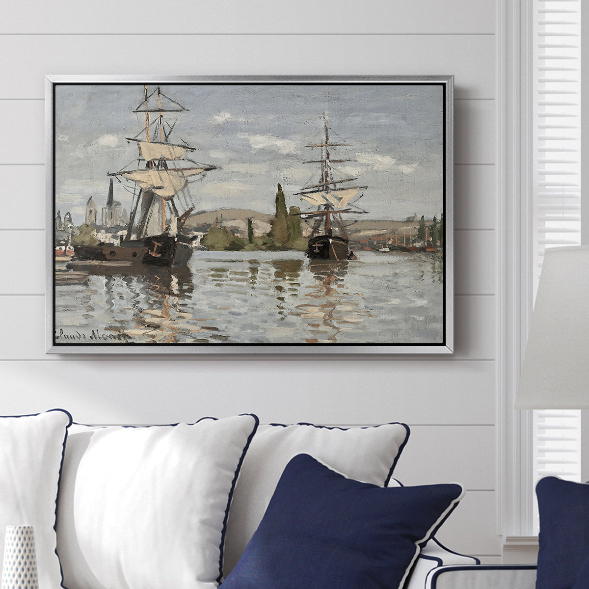 Ships Riding on the Seine at Rouen, 1872 by Claude Monet displayed above a sofa in a living room in a silver floater frame, featuring an impressionist river scene with anchored sailing ships and reflections.