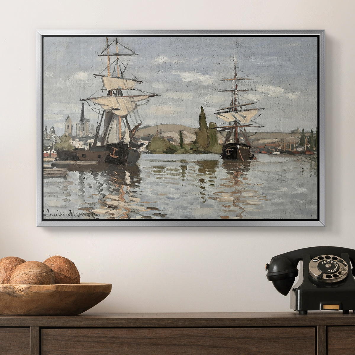 Ships Riding on the Seine at Rouen, 1872 by Claude Monet in a silver floater framed canvas displayed above a console table in a hallway, featuring a nautical landscape with vessels resting on calm water.