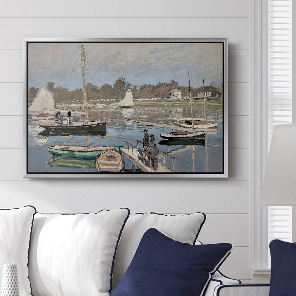 The Basin at Argenteuil, 1874 by Claude Monet displayed above a sofa in a living room in a silver floater frame, featuring an impressionist boating scene with clustered masts and gentle ripples.