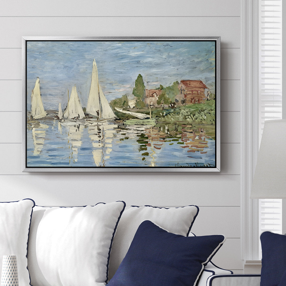 Regatta at Argenteuil, 1872 by Claude Monet displayed above a sofa in a living room in a silver floater frame, featuring a lively regatta scene with multiple boats and fluttering sails.